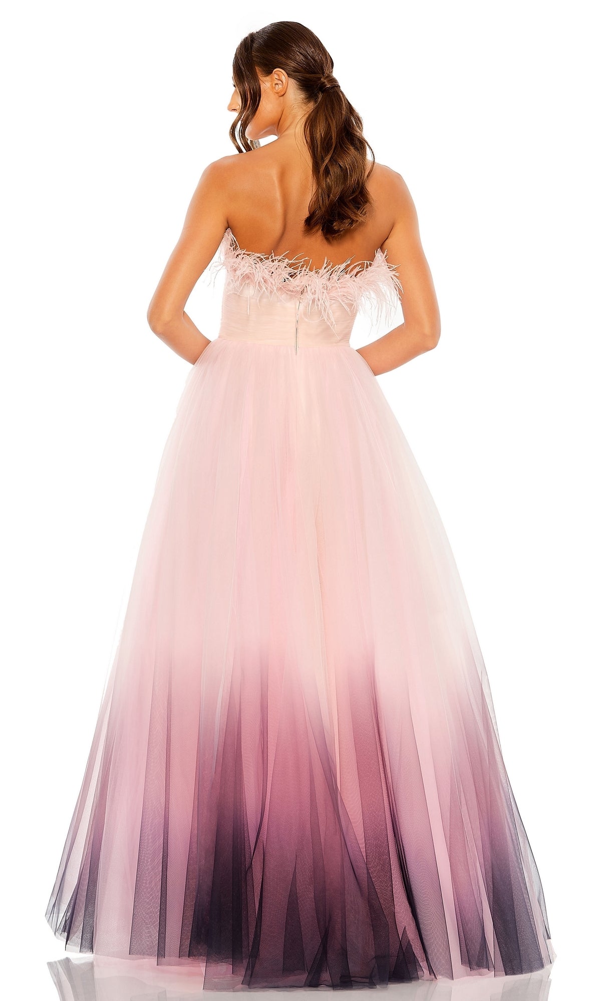 A woman faces away from the camera in the Long Formal Dress 20557 by Mac Duggal, featuring a strapless ball gown silhouette with ombre pink-to-purple tulle and delicate feather details at the bodice.